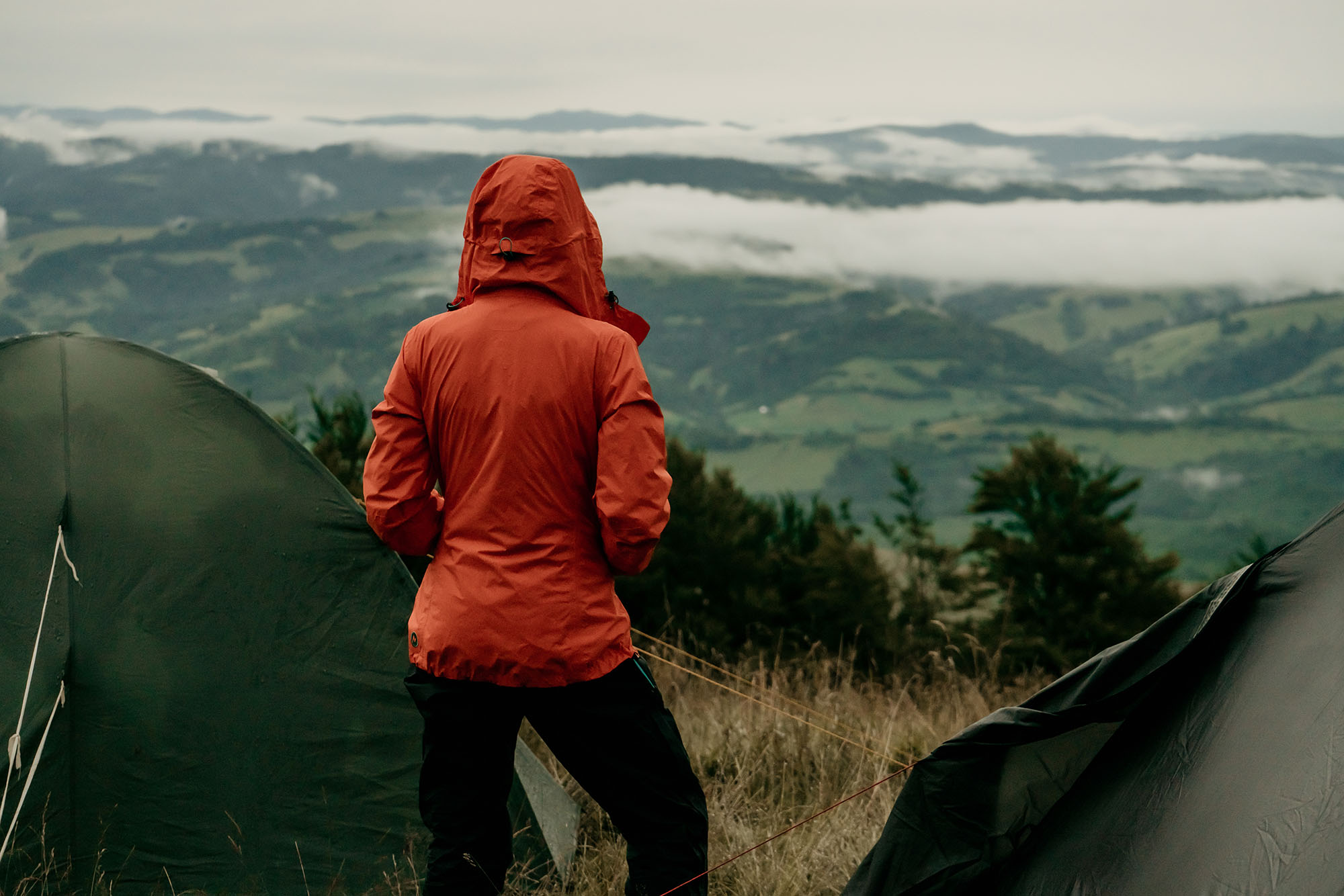 Back view of female tourist in orange jacket with rucksack looking at beautiful scenery of mountains, young hipster backpacker exploring nature landscape and environment during journey