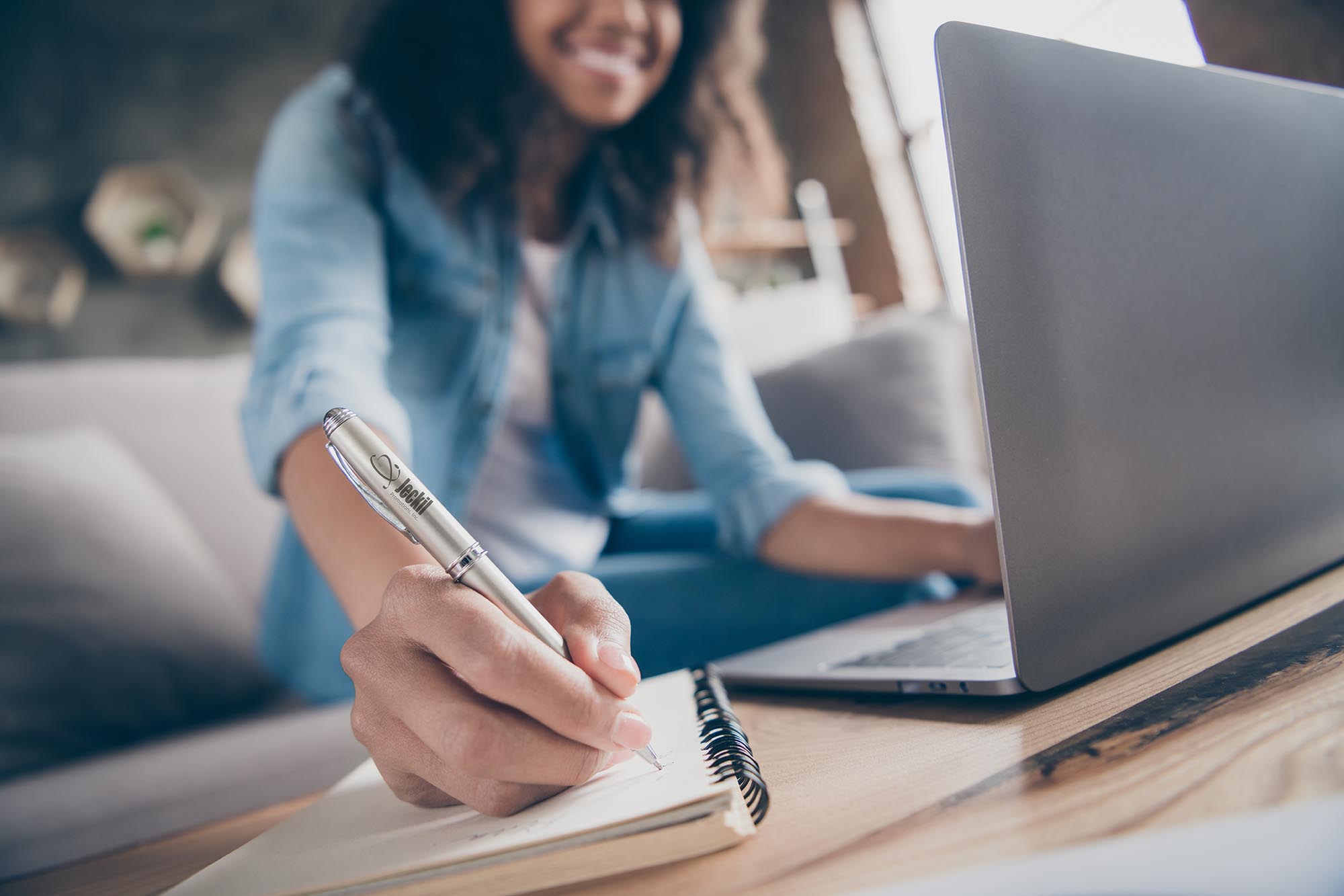 Cropped blurry focus photo of amazing dark skin curly lady browsing notebook, writing pen plan list diary sitting cozy sofa wear casual denim outfit flat indoors