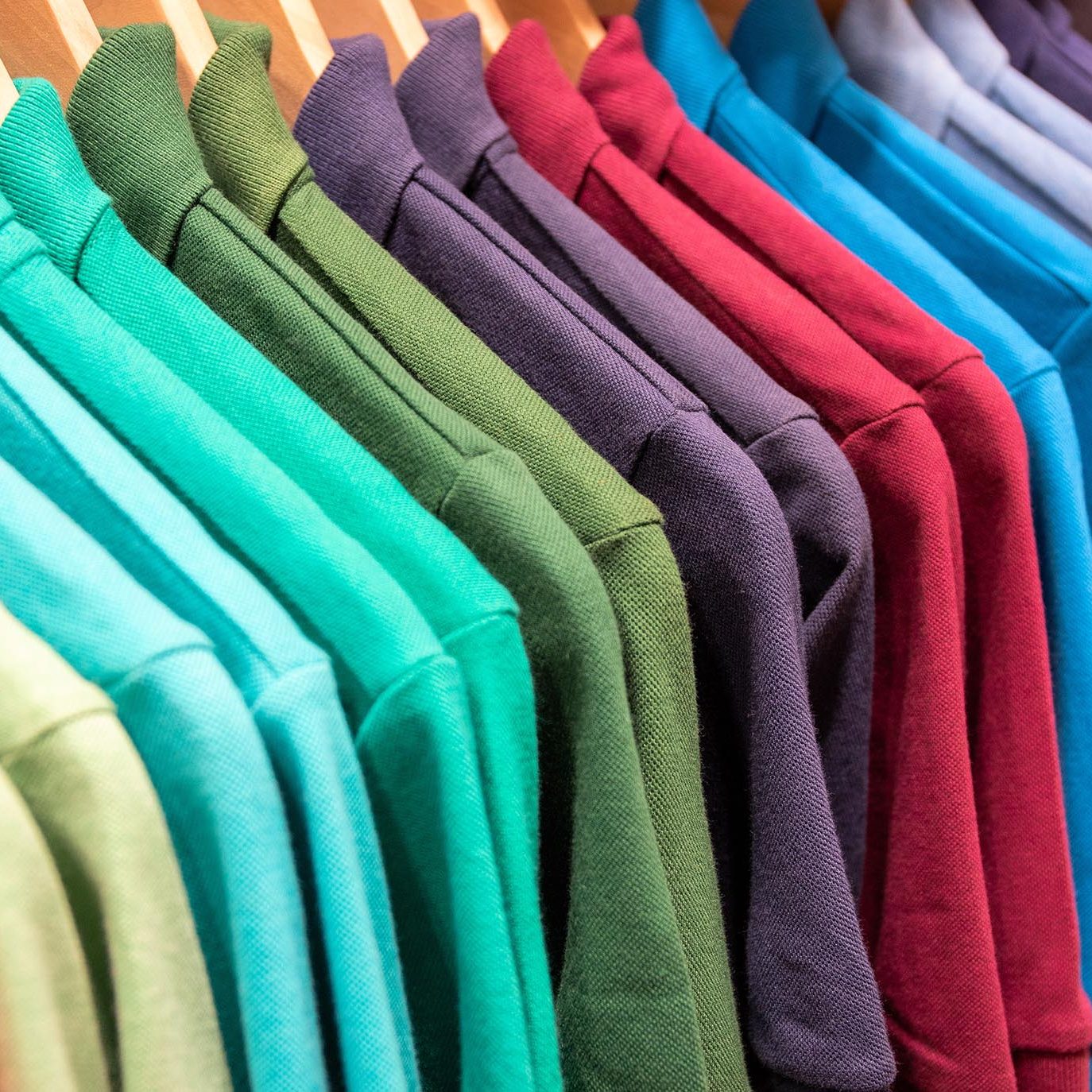 Vibrant shirts on hangs for sale in shop. Multicolored polo on wooden hanger. Summer fashion in department store Vibrant shirts on hangs for sale in shop. Multicolored polo on wooden hanger. Summer fashion in department store. Unisex apparel for warm weather. Sale in shopping mall. Color gradient t-shirts